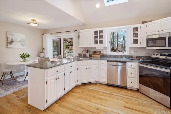 a kitchen with stainless steel appliances granite countertop a stove a sink dishwasher and white cabinets with wooden floor