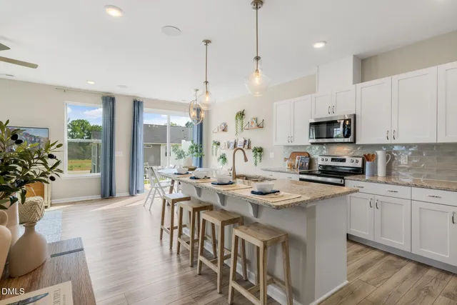 a kitchen with stainless steel appliances granite countertop a stove a refrigerator a kitchen island a sink and white cabinets with wooden floor