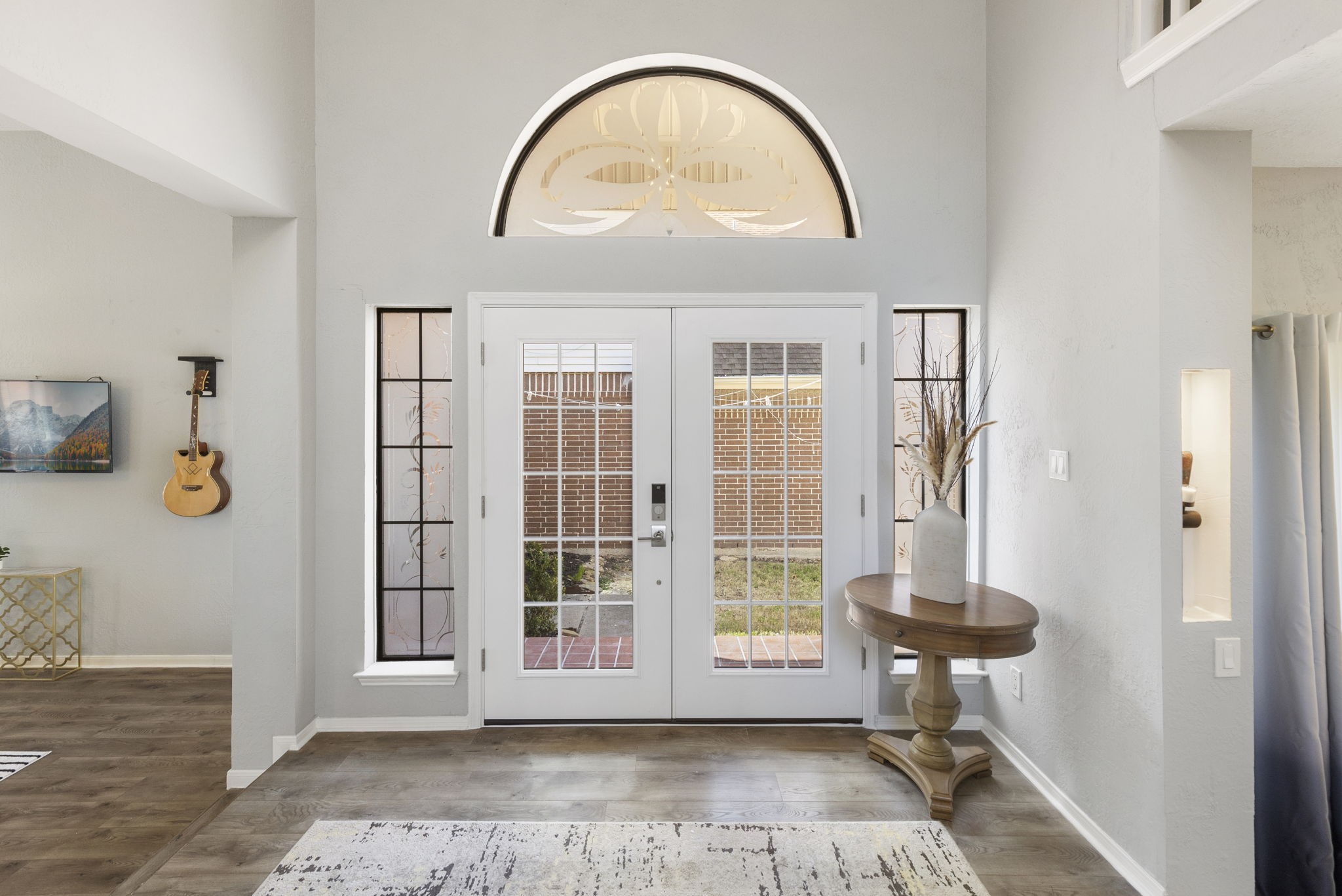2110 Paso Rello Drive Houston, TX 77077 - Photo 5 of 41 This inviting entryway features a high ceiling and abundant natural light from large windows surrounding the front door. A decorative window above adds elegance, while the space includes stylish wood flooring and a small table for decor.