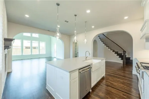 a large white kitchen with a large island oven a stove a dining table and chairs with wooden floor