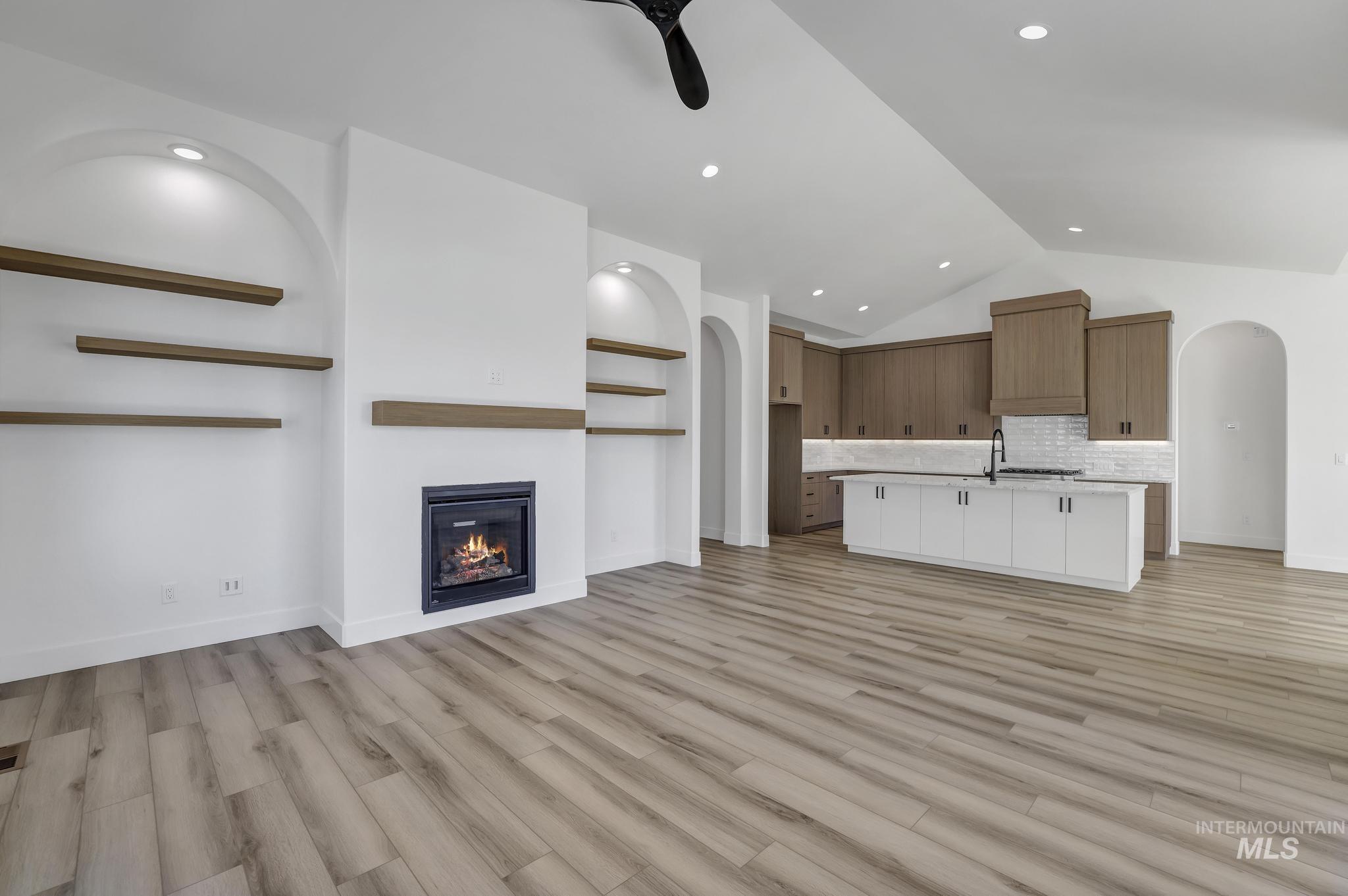 521 Falling Leaf Lane Twin Falls, ID 83301 - Photo 13 of 42 Unfurnished living room with arched walkways, light wood-type flooring, a glass covered fireplace, vaulted ceiling, and recessed lighting