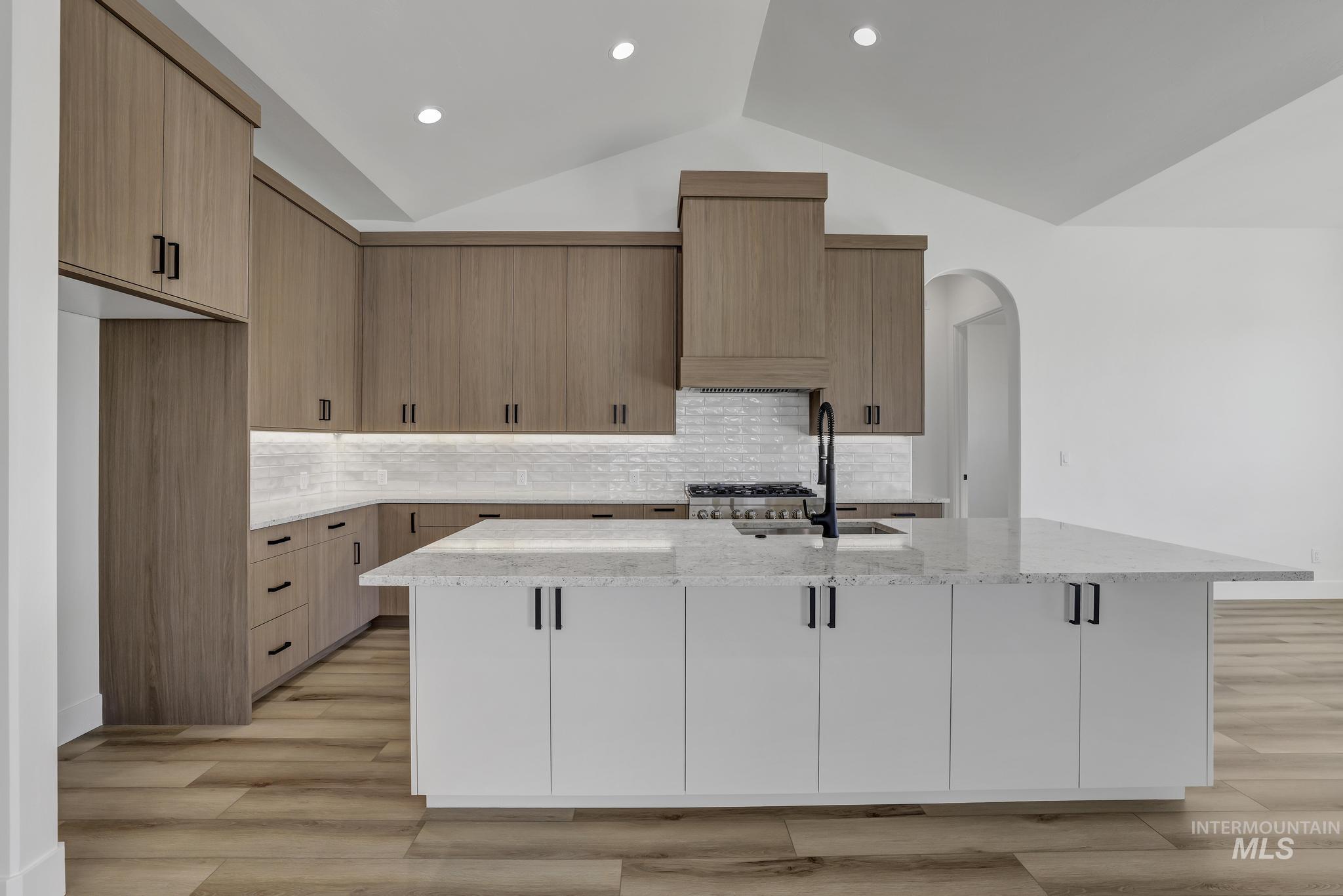 521 Falling Leaf Lane Twin Falls, ID 83301 - Photo 14 of 42 Kitchen with light stone countertops, vaulted ceiling, light wood finished floors, a center island with sink, and arched walkways