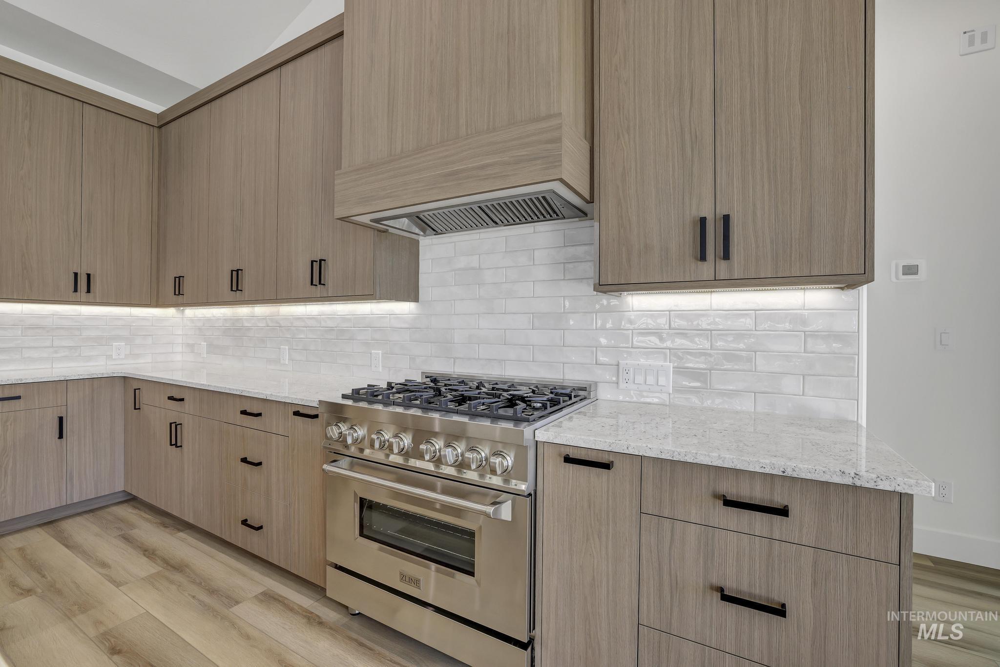 521 Falling Leaf Lane Twin Falls, ID 83301 - Photo 16 of 42 Kitchen with high end range, light stone counters, light wood-style flooring, premium range hood, and decorative backsplash