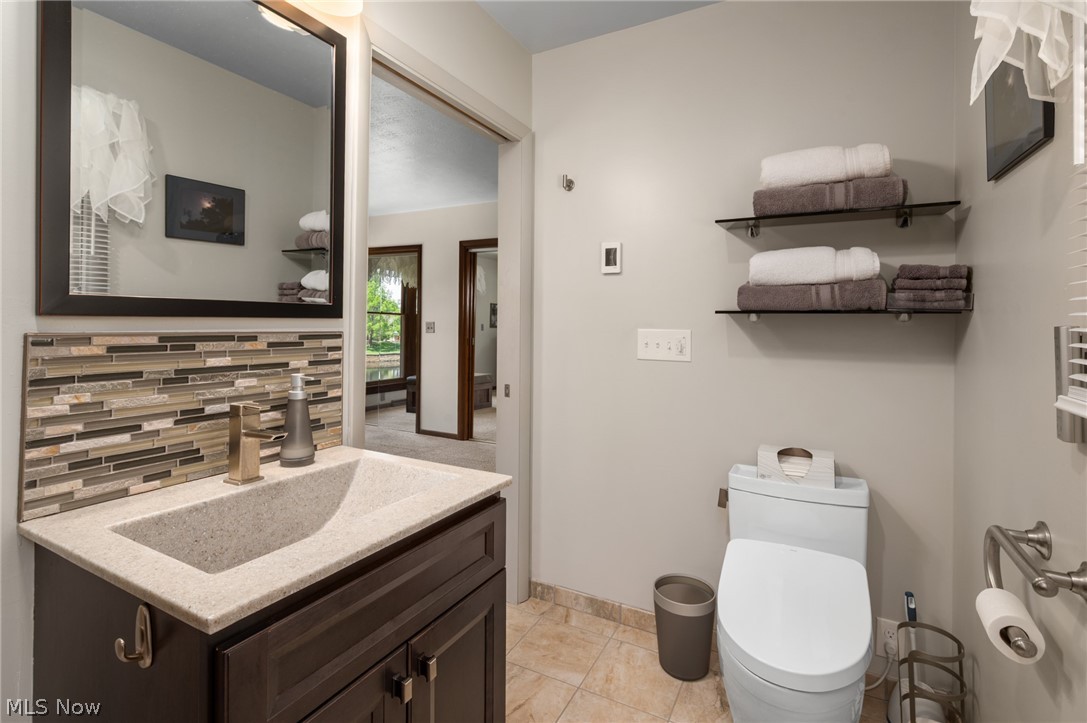 685 Sunnyside Road Vermilion, OH 44089 - Photo 23 of 50 Bathroom featuring a dark wood-finish vanity with a light speckled countertop, an integrated rectangular sink, a contemporary faucet, and a horizontal mosaic tile backsplash