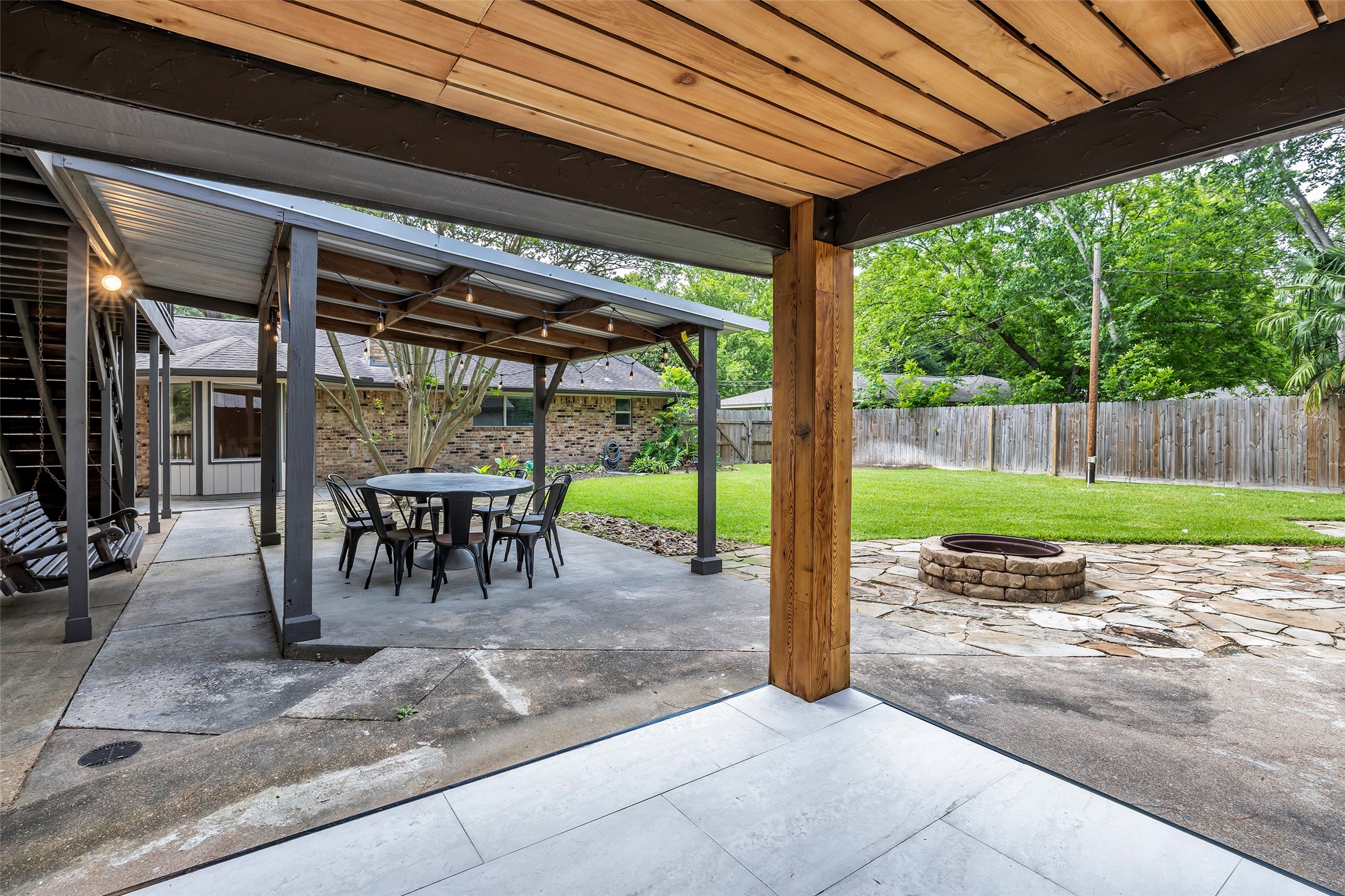 22502 Fields Lane Spring, TX 77389 - Photo 35 of 39 This outdoor space features a covered patio with seating, a swing, and a stone fire pit. The area is surrounded by a well-maintained lawn and privacy fence, perfect for relaxation and entertaining.