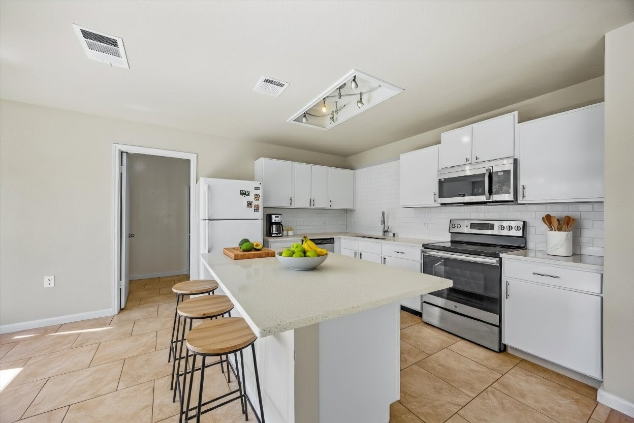 7541 Redrick Drive Austin, TX 78747 - Photo 11 of 40 Kitchen featuring decorative backsplash, stainless steel appliances, white cabinets, and a kitchen bar