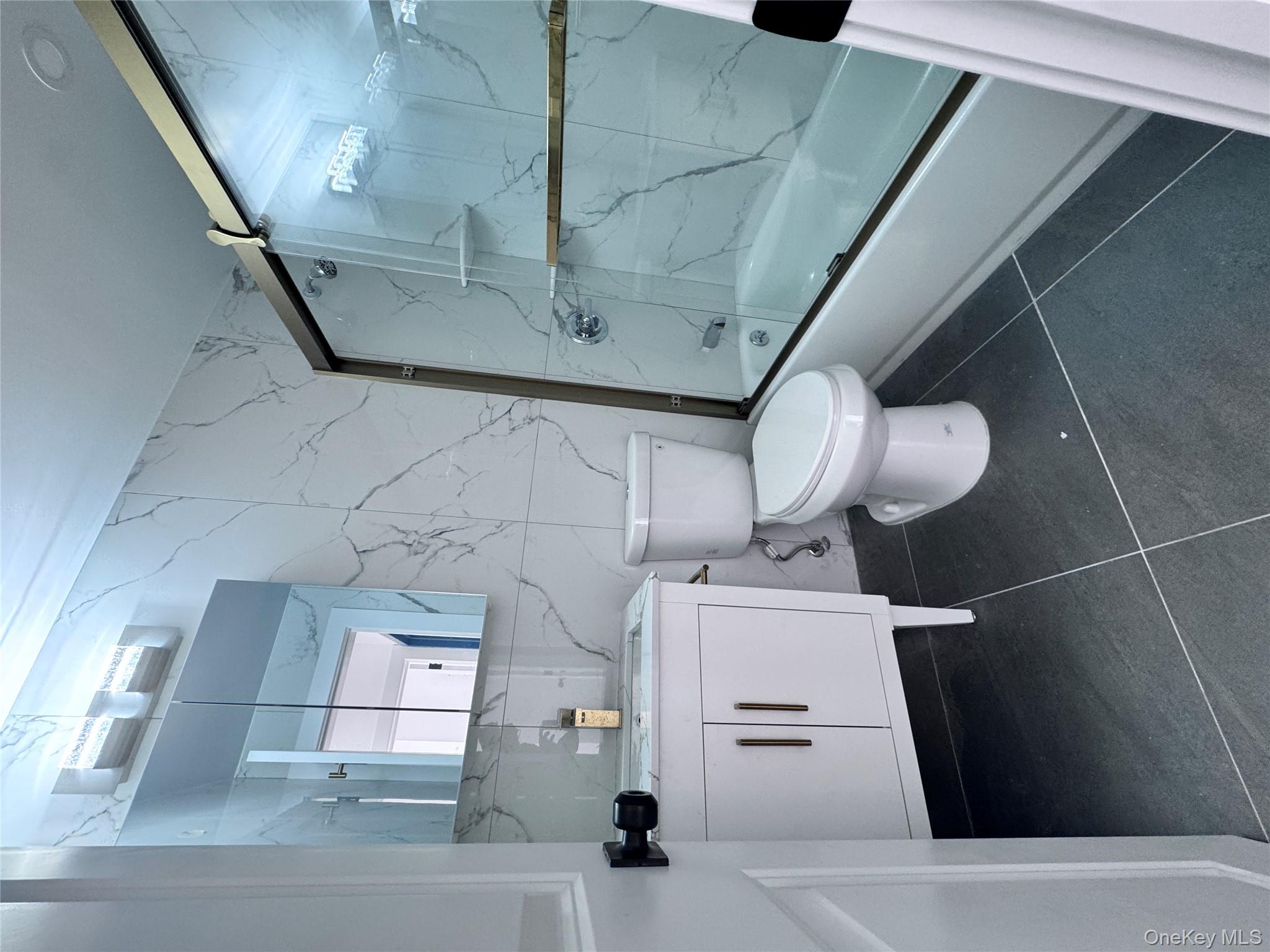 41-05 45th Street, Unit 2B Queens, NY 11103 - Photo 3 of 5 Bathroom featuring vanity, bath / shower combo with glass door, dark tile patterned flooring, tile walls, and stone wall