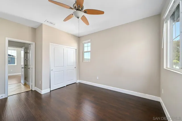 an empty room with wooden floor fan and windows
