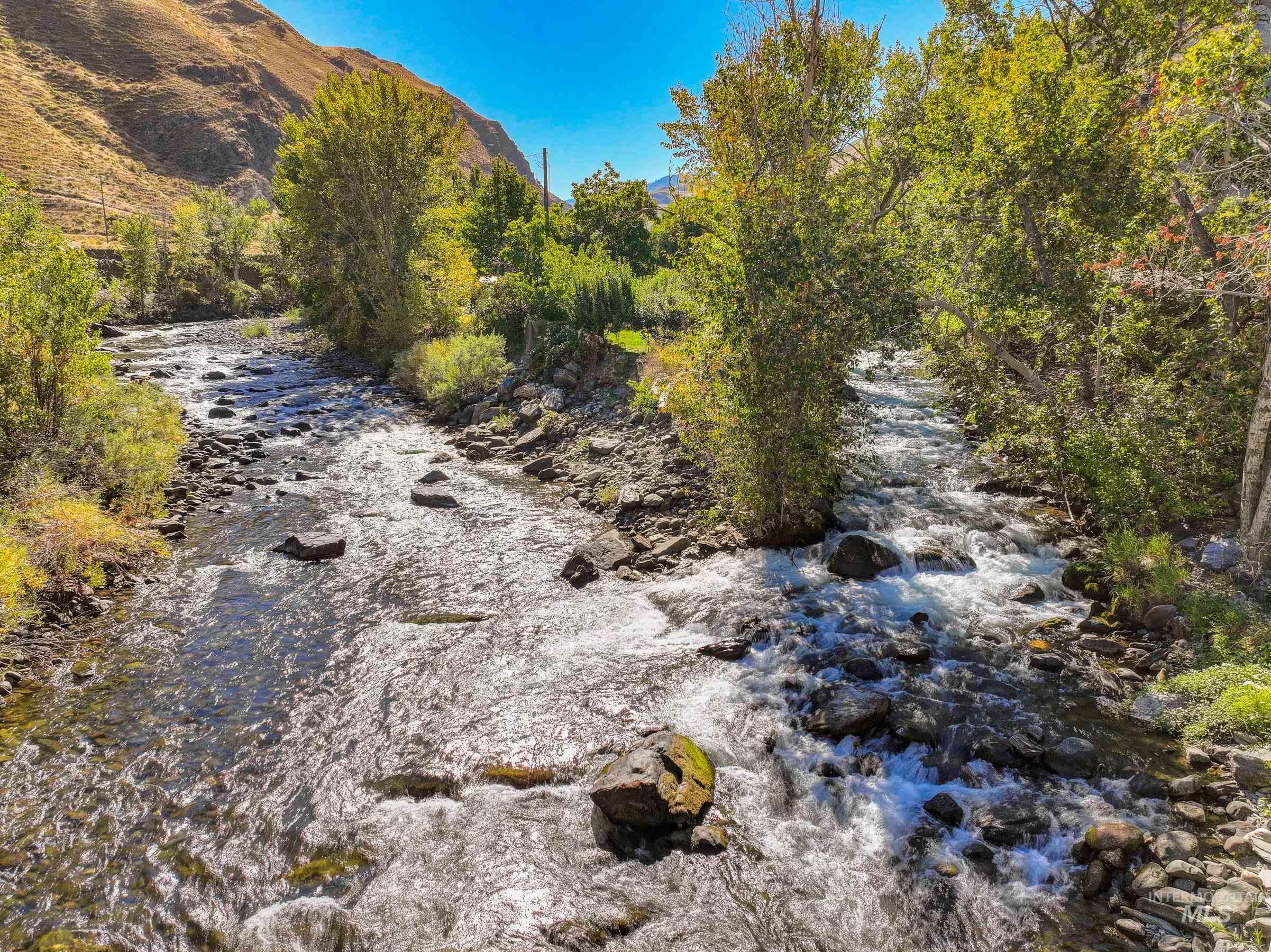 7026 S Highway Riggins, ID 83549 - Photo 2 of 50 Flowing river with rocky bed, bordered by lush green foliage and distant hills
