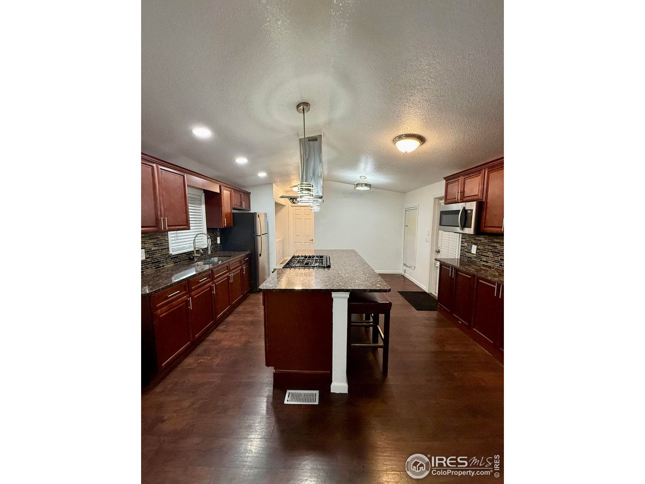 9775 Lark Street Federal Heights, CO 80260 - Photo 5 of 17 a kitchen with stainless steel appliances kitchen island granite countertop a stove a refrigerator a sink a dining table and chairs with wooden floor