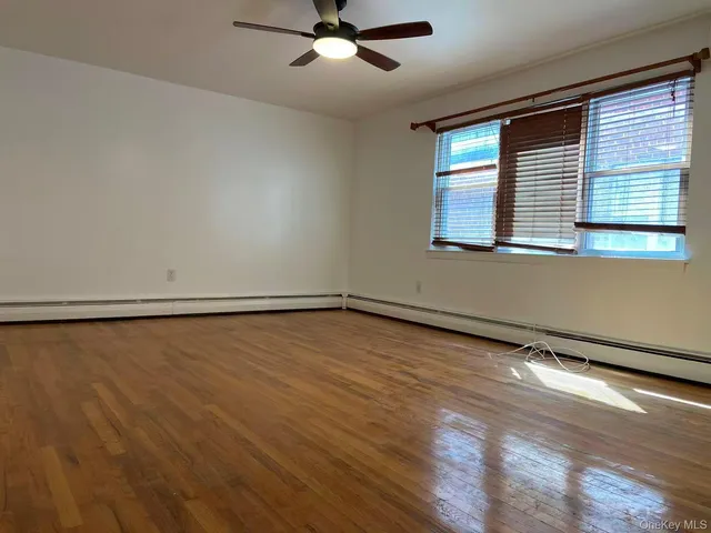 a view of an empty room with wooden floor and fan