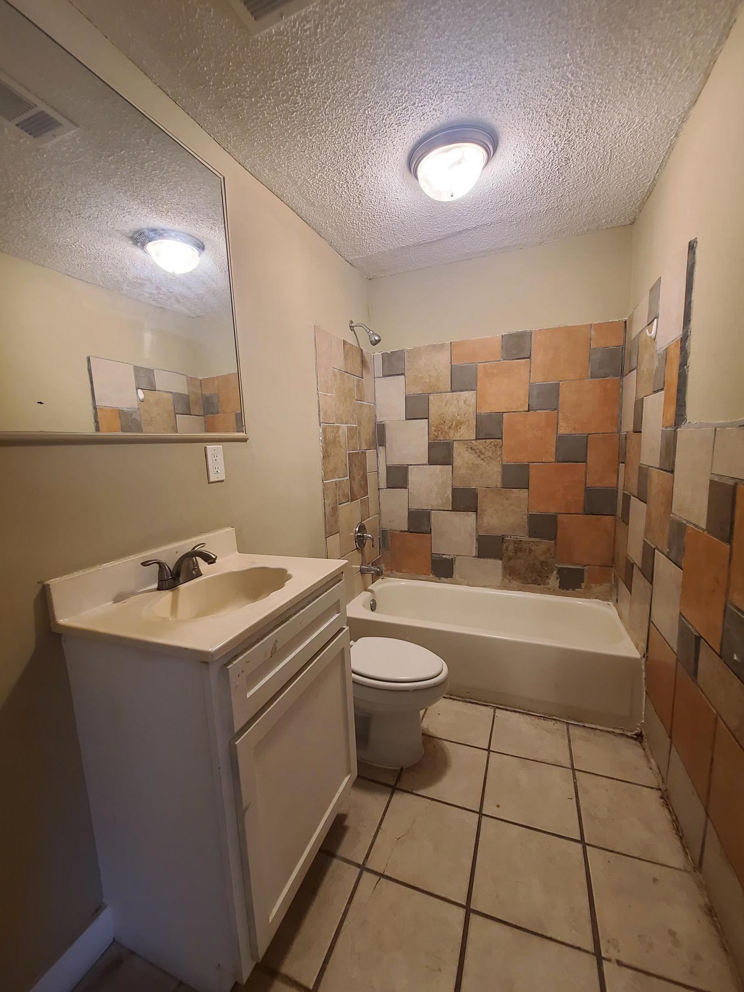 Bathroom featuring a single vanity, integrated sink, bathtub, and tiled shower surround