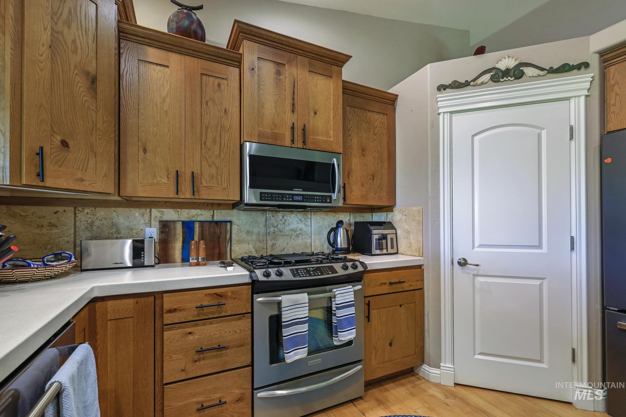 100 Olympic Road Jerome, ID 83338 - Photo 16 of 50 Kitchen featuring wood cabinetry, light-toned countertops, tile backsplash, stainless steel gas range, and an over-the-range microwave