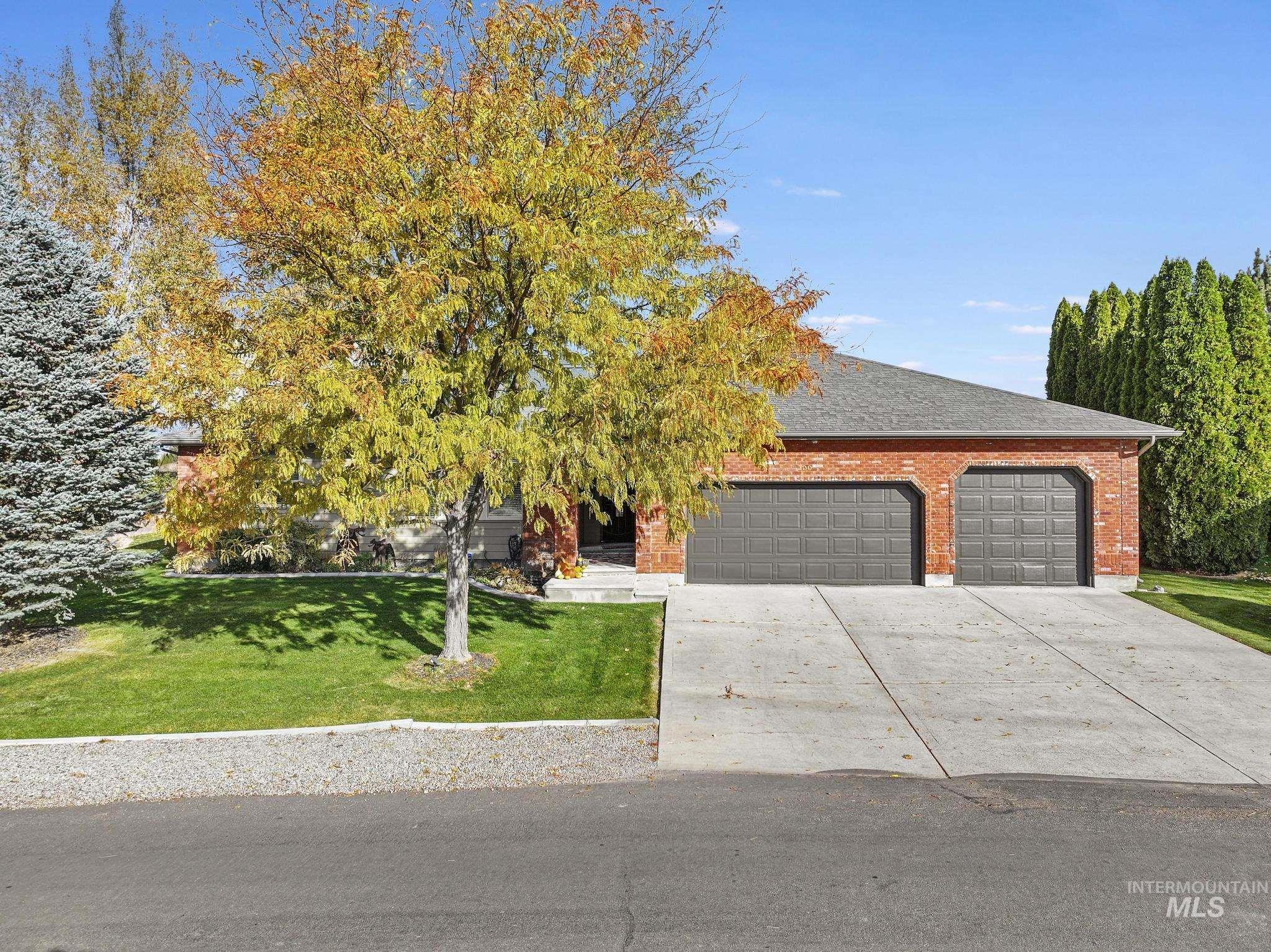 100 Olympic Road Jerome, ID 83338 - Photo 49 of 50 Brick exterior home featuring a two-car garage, concrete driveway, and a manicured lawn with mature trees