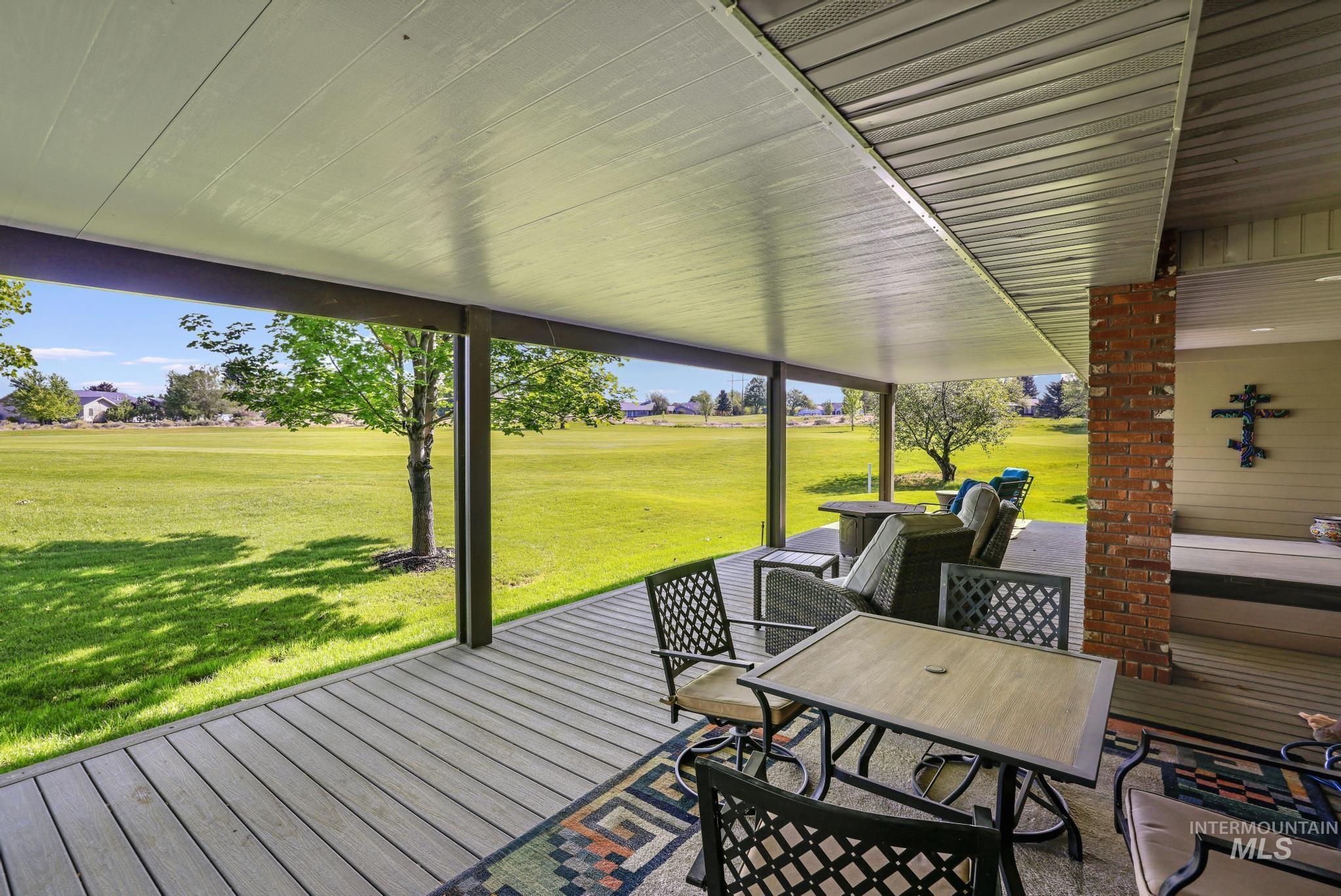 100 Olympic Road Jerome, ID 83338 - Photo 5 of 50 Covered patio with composite decking, exposed brick column, and a light-colored soffit ceiling overlooking an expansive green space with mature trees