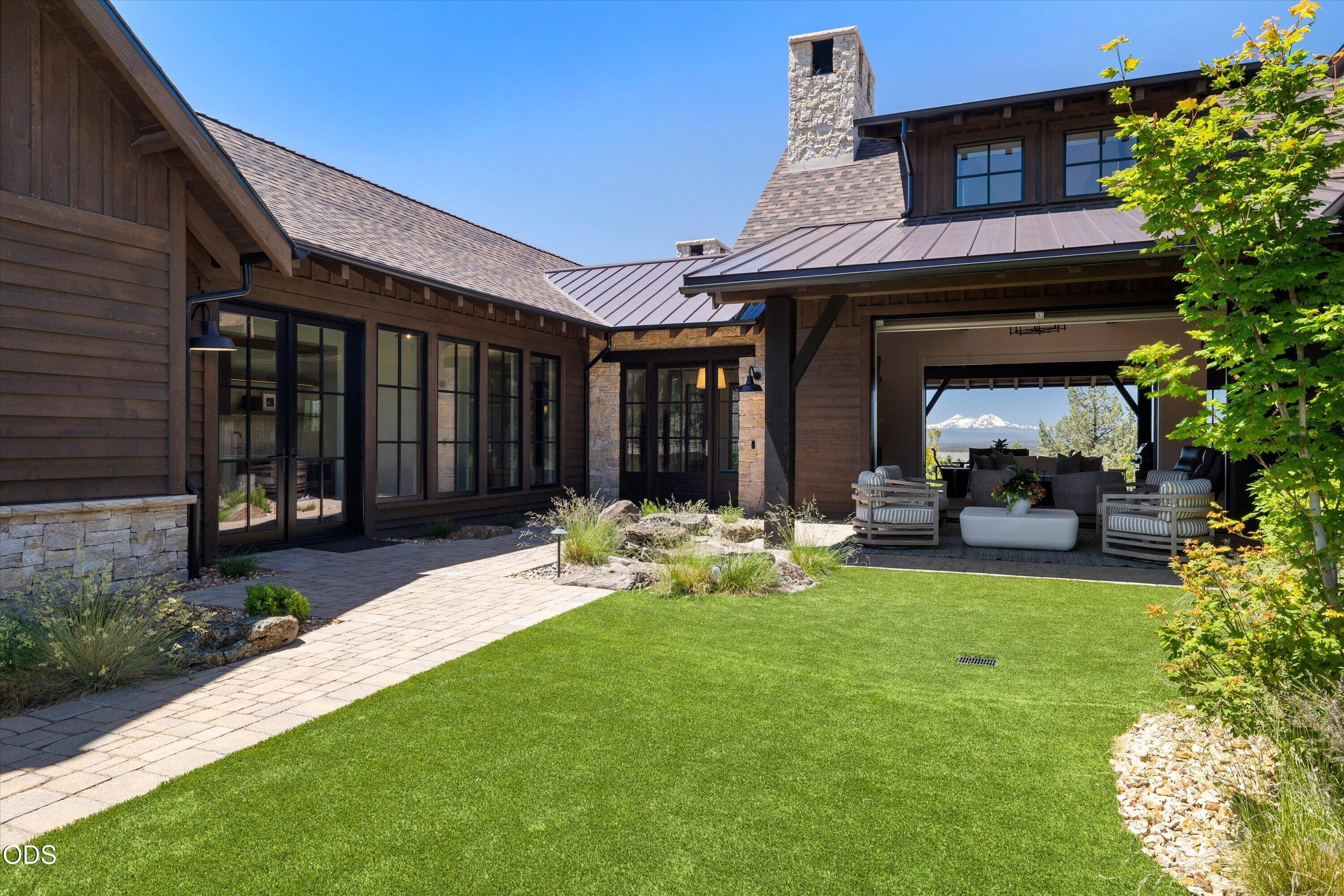 16215 South W Vaqueros Way Powell Butte, OR 97753 - Photo 4 of 48 Courtyard featuring pavers, easy landscape, covered patio, views through the home to the mountains beyond, tranquil Montana Moss rock water feature, and doors to the guest suites