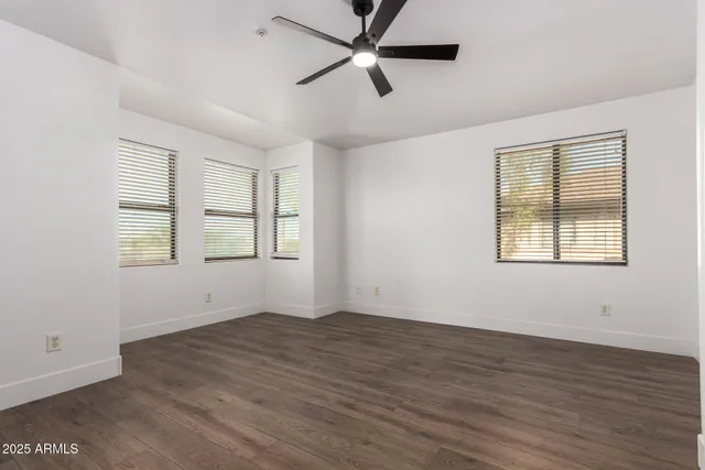 an empty room with wooden floor ceiling fan and windows