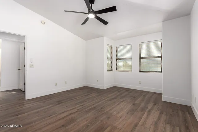 an empty room with wooden floor ceiling fan and windows