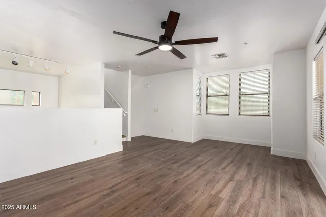 an empty room with wooden floor ceiling fan and windows