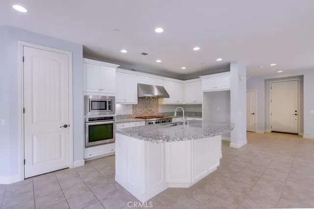 a large kitchen with stainless steel appliances granite countertop a stove a sink a refrigerator and white cabinets