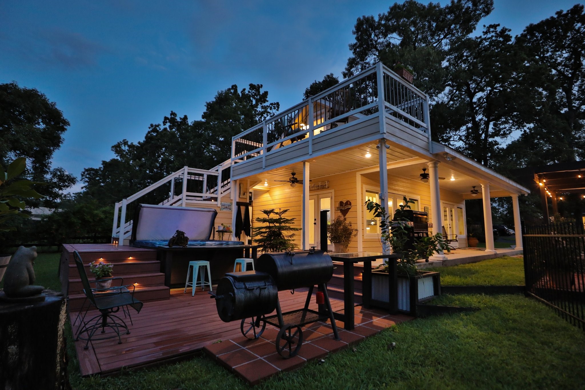 34310 High Point Drive Magnolia, TX 77355 - Photo 26 of 48 Inviting sunset view of the 1,000 guest home features a spacious two-level deck with ample outdoor seating, a hot tub, and a grill area, perfect for entertaining. The well-lit patio and surrounding greenery create a cozy ambiance for evening gatherings.