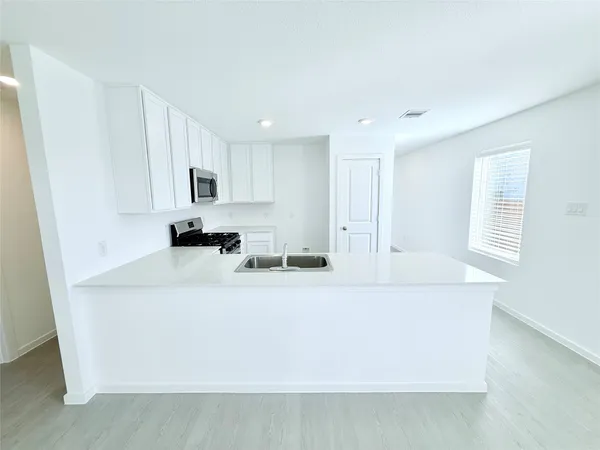 a living room with stainless steel appliances white cabinets a couch a stove a chimney a sink and a window