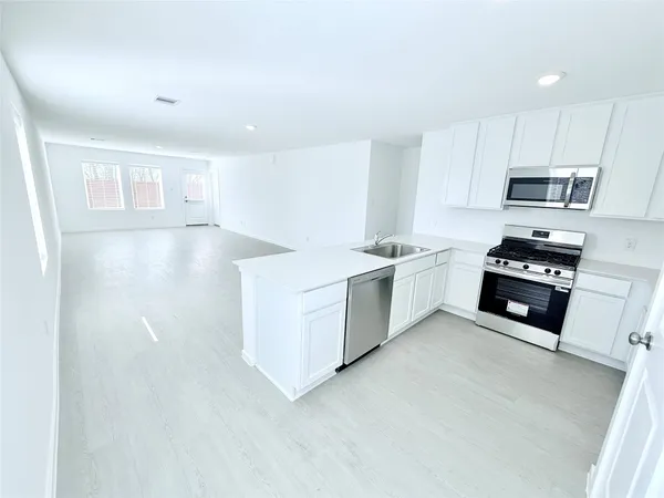 a kitchen with stainless steel appliances a sink a stove a microwave a refrigerator a sink and cabinets