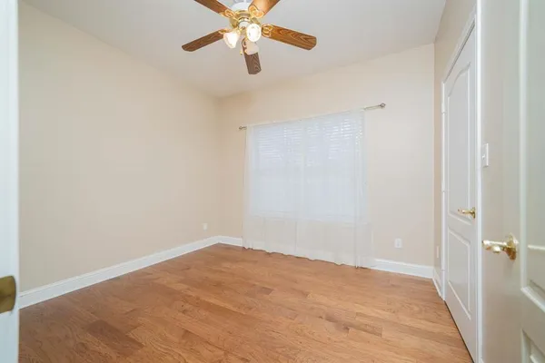 an empty room with a chandelier fan and wooden floor