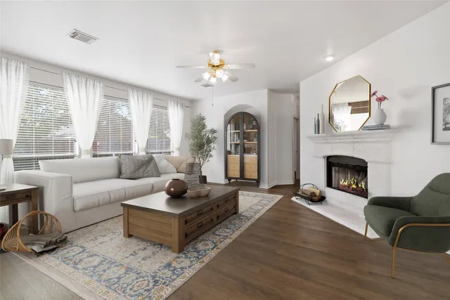 an empty room with wooden floor a ceiling fan a fireplace and windows