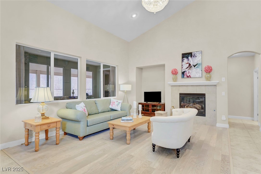 9725 Sandy Turtle Avenue Las Vegas, NV 89149 - Photo 6 of 51 Living area featuring high vaulted ceiling, arched walkways, a tile fireplace, and light wood-style floors