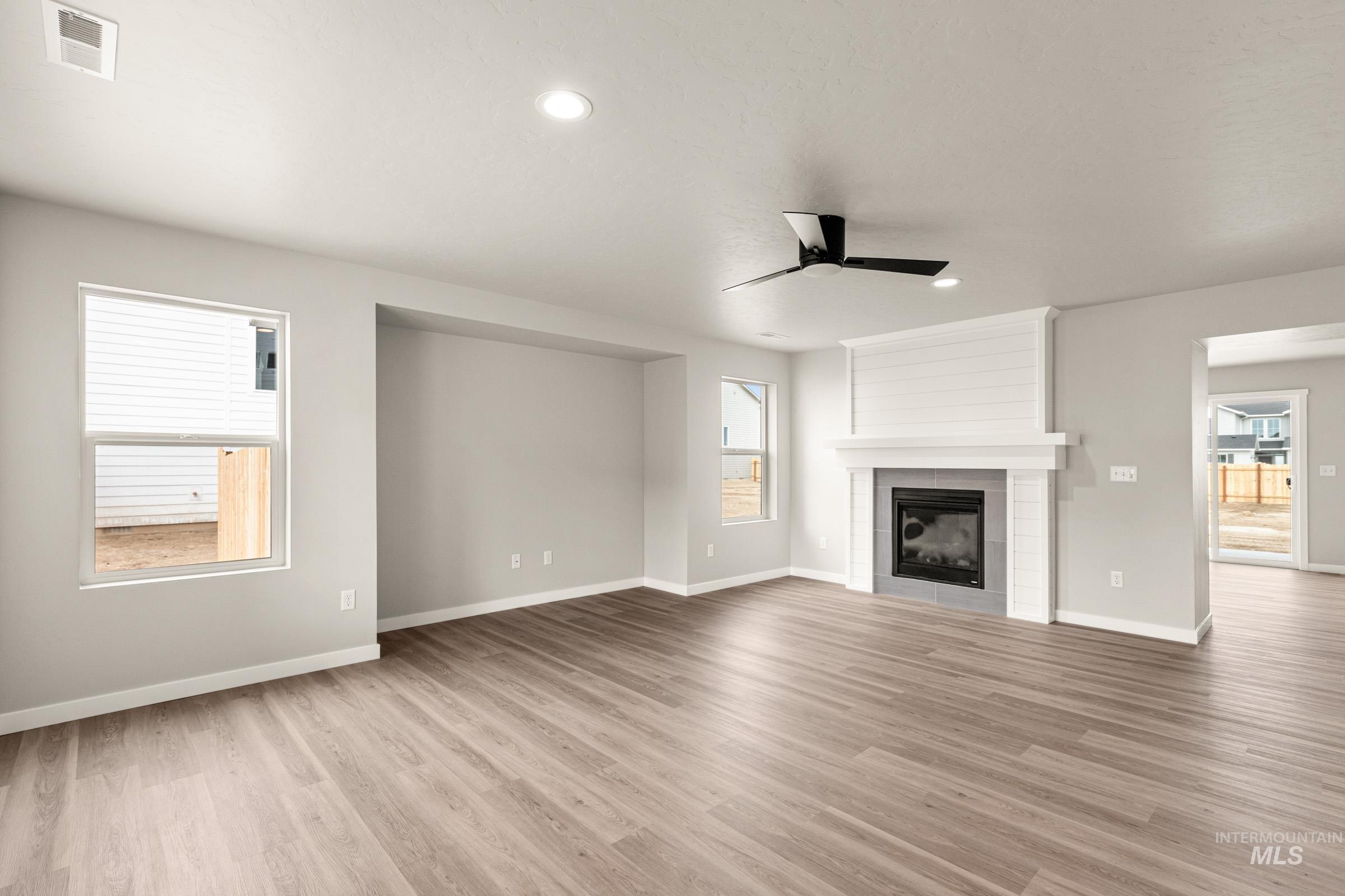 13686 Inman Court Caldwell, ID 83607 - Photo 8 of 20 Unfurnished living room featuring ceiling fan, healthy amount of natural light, light wood-style flooring, a tile fireplace, and recessed lighting