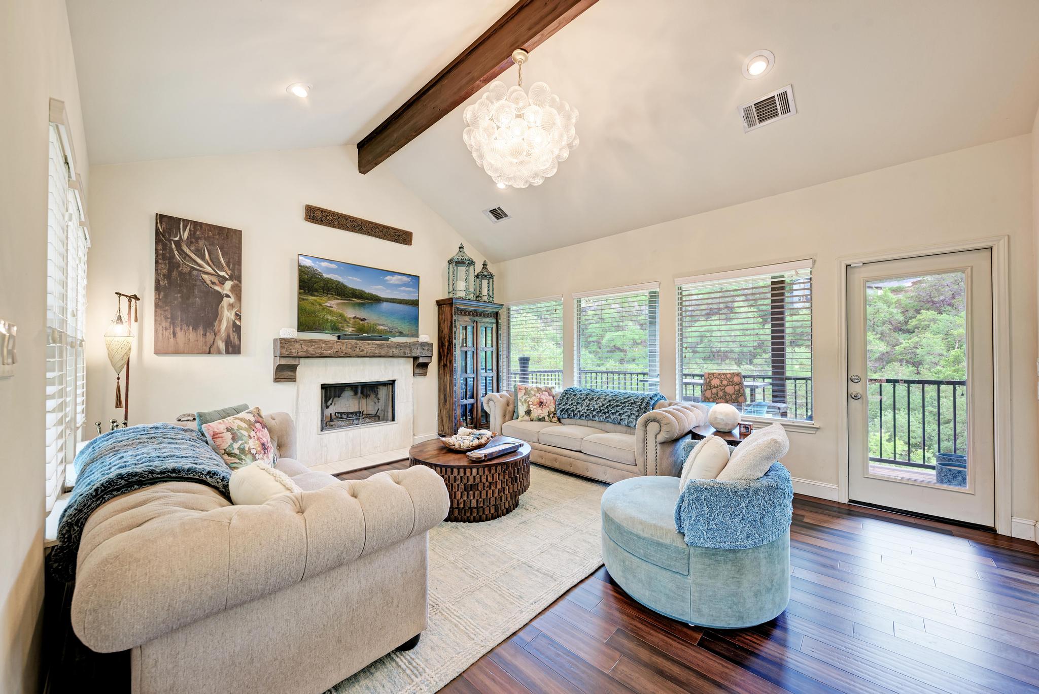 2605 Indian Creek Road Austin, TX 78734 - Photo 3 of 33 Spacious living area featuring a vaulted ceiling with exposed wood beam, a fireplace with a stone surround and wood mantel, expansive windows, a glass-paneled door, and wood-finish flooring