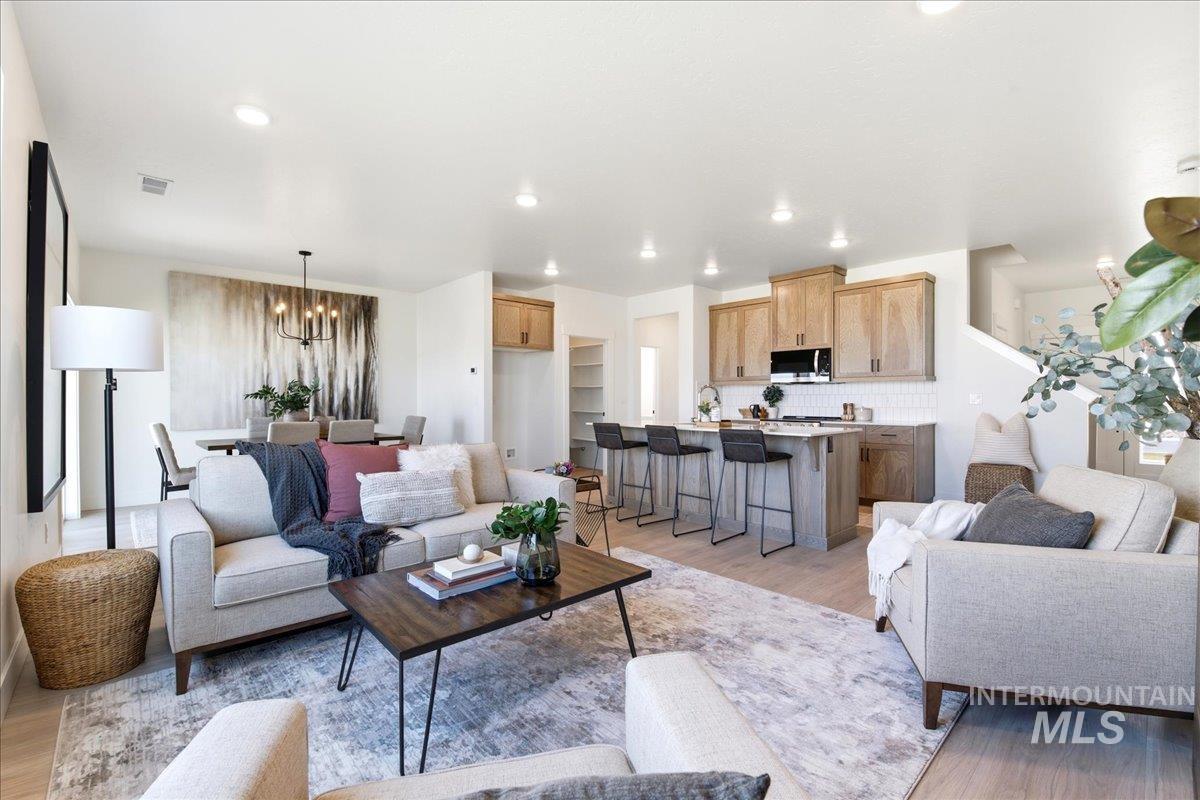 3405 Elliptical Lane Caldwell, ID 83607 - Photo 4 of 17 Open-concept living space featuring wood-finish flooring, recessed lighting, a kitchen island with seating, a subway tile backsplash, and light wood cabinetry