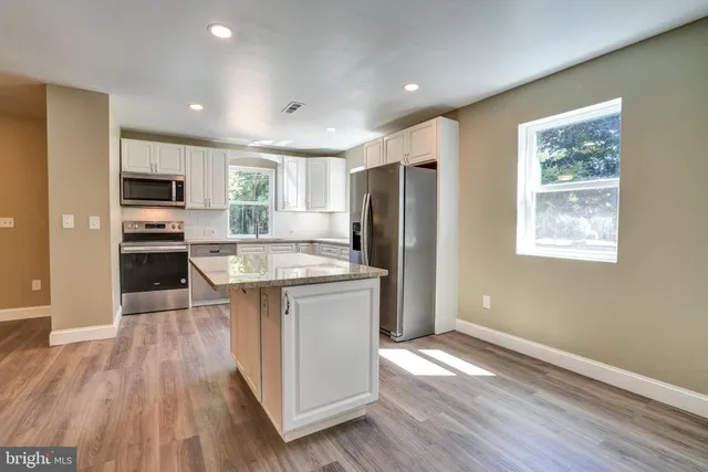 a kitchen with stainless steel appliances granite countertop a refrigerator a stove top oven a sink dishwasher and wooden floor