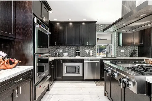 a kitchen with stainless steel appliances granite countertop a stove a sink dishwasher and a microwave oven with wooden cabinets