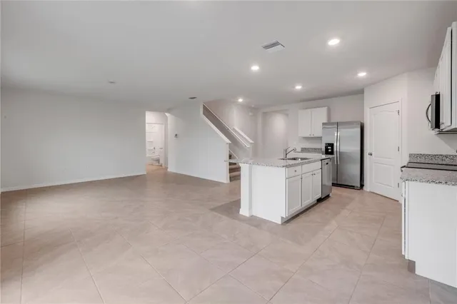 a large white kitchen with stainless steel appliances granite countertop a stove a sink a refrigerator and white cabinets with wooden floor