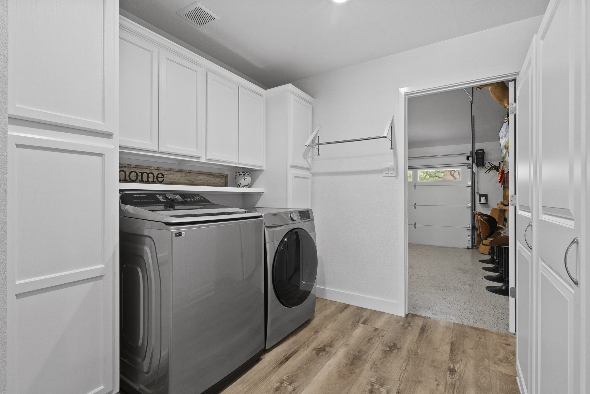 2802 Robin Road Manchaca, TX 78652 - Photo 13 of 40 Laundry area featuring wood-finish flooring, white shaker cabinetry, a white floating shelf, and a wall-mounted drying rack