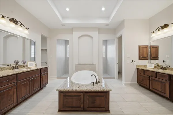 a spacious bathroom with a granite countertop double vanity sink a mirror and a bathtub