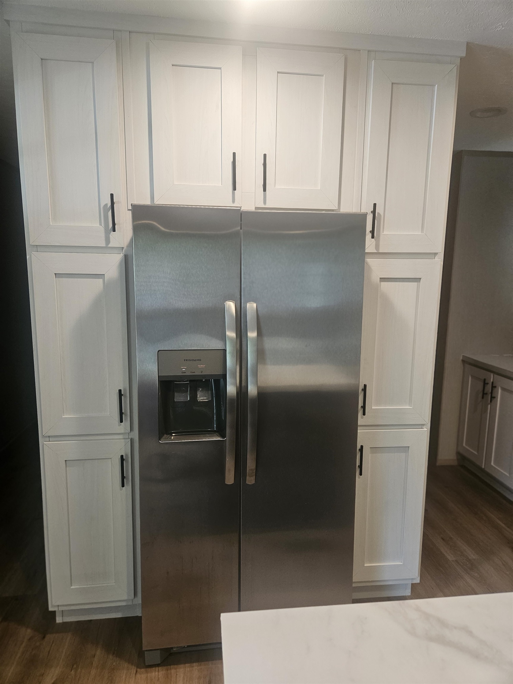75 Pittman Road, Unit ROAD Somerville, TN 38068 - Photo 10 of 26 Stainless steel side-by-side refrigerator with exterior ice and water dispenser, flanked by white shaker-style cabinetry with black hardware, wood-finish flooring, and a white countertop