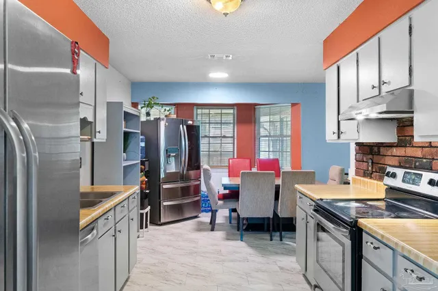 a kitchen with granite countertop a refrigerator stove top oven dining table and chairs