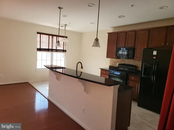 a kitchen with stainless steel appliances granite countertop a refrigerator a sink dishwasher a stove and a dining table with wooden floor