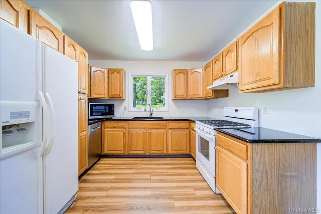 a kitchen with stainless steel appliances granite countertop a refrigerator a sink dishwasher a stove and a dining table with wooden floor