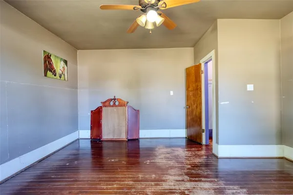 a view of an empty room with wooden floor and a ceiling fan