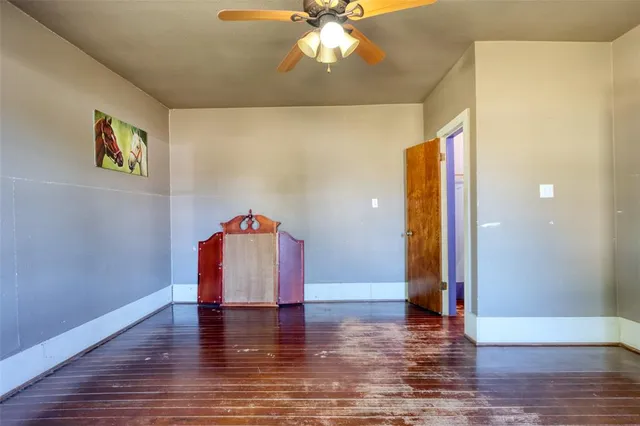 a view of an empty room with wooden floor and a ceiling fan