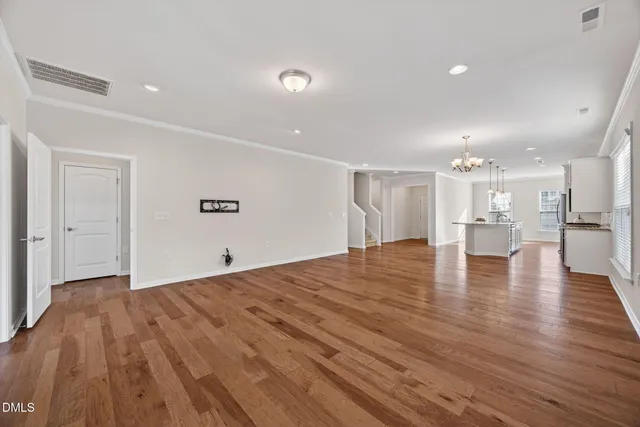 a view of an empty room with wooden floor and a kitchen