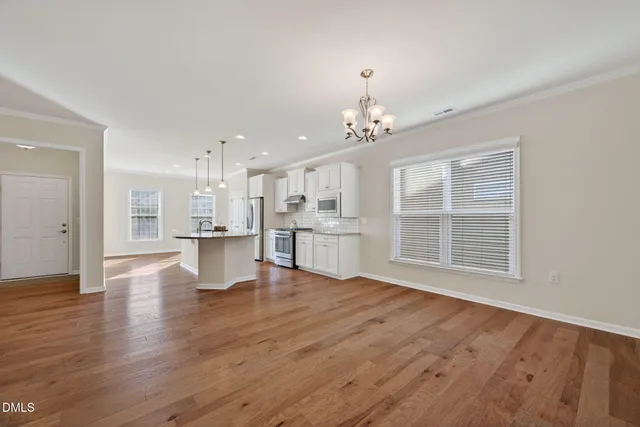 a view of an empty room with wooden floor and a kitchen