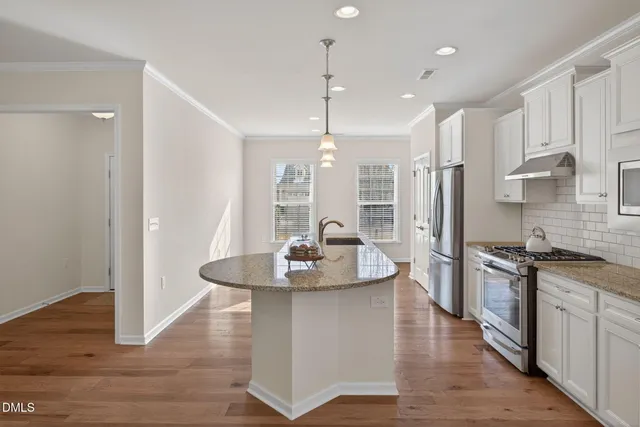 a kitchen with stainless steel appliances granite countertop a stove a sink dishwasher a refrigerator and white cabinets with wooden floor