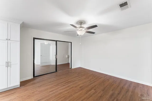 an empty room with wooden floor fan and windows