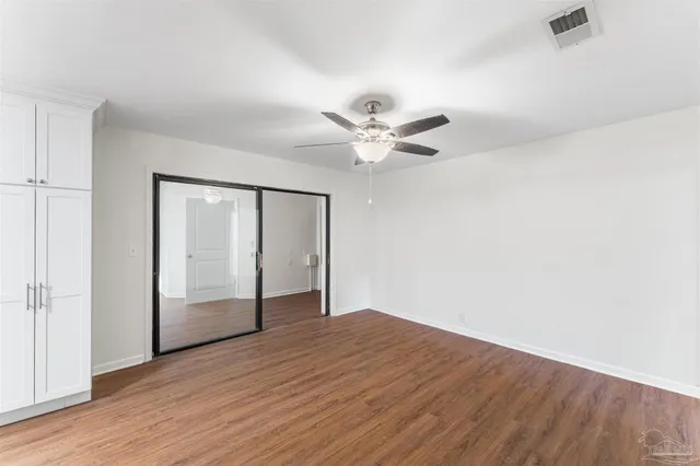 an empty room with wooden floor fan and windows