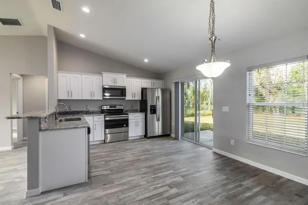 a kitchen with stainless steel appliances granite countertop a refrigerator a sink dishwasher a oven and a dining table with wooden floor